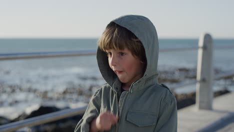 portrait playful little caucasian boy enjoying ocean seaside wearing jacket on windy sunny day slow motion