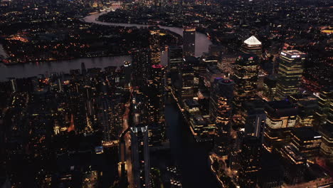 Forwards-fly-above-night-city,-modern-business-urban-district-with-skyscrapers.-Tilt-up-reveal-of-cityscape-at-dusk.-London,-UK