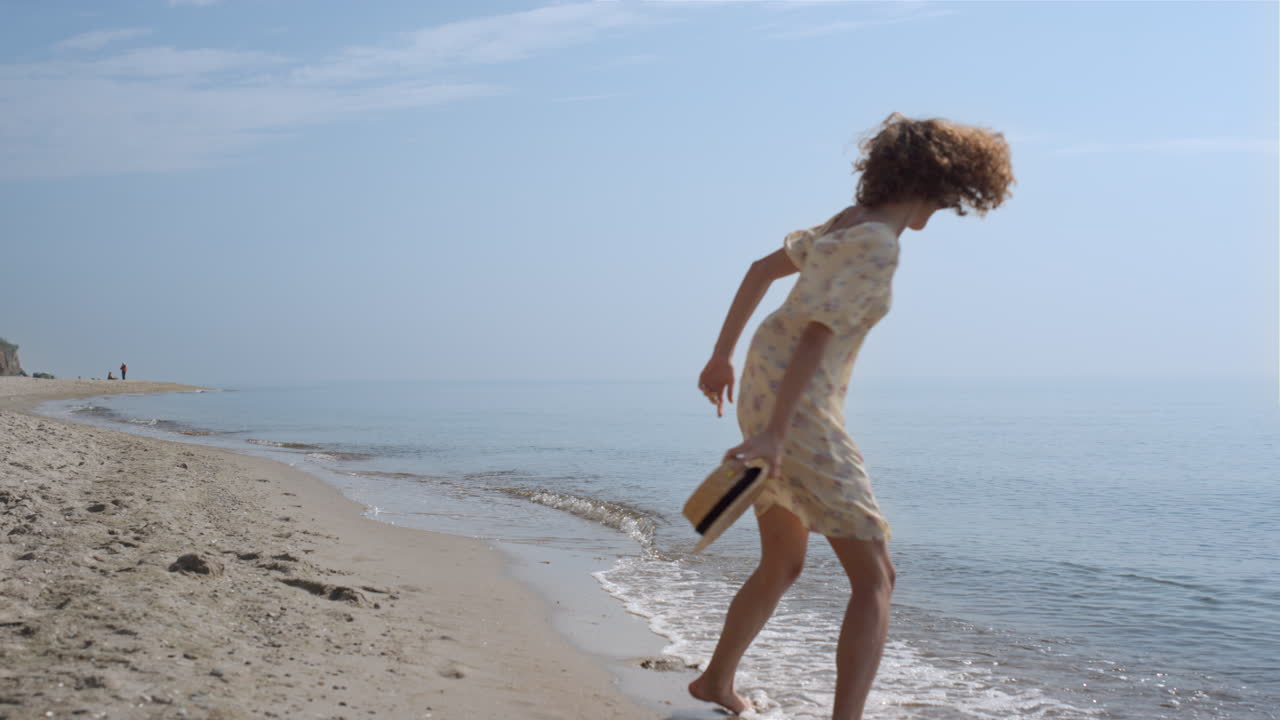 Ragazza serena si diverte in spiaggia in una giornata estiva. Donna che ride e gira sulle onde dell'oceano.
