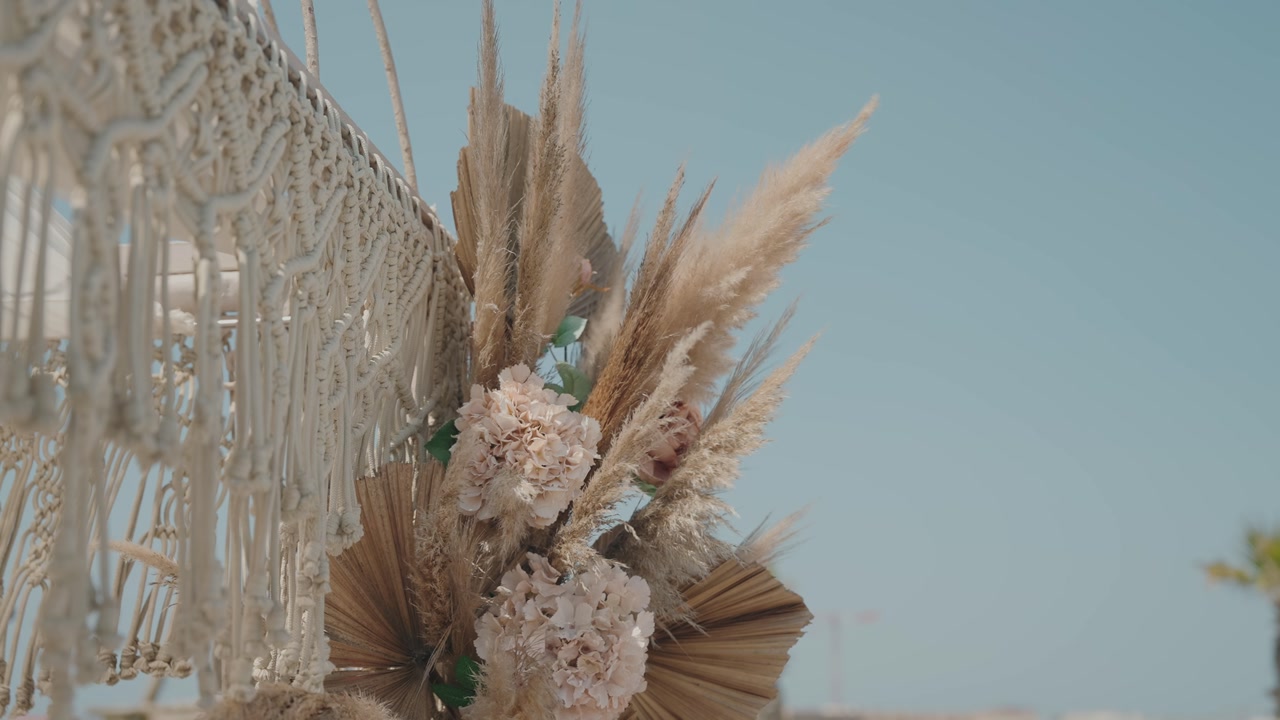 bohemian wedding arch decorated with pampas grass flowers and macrame details under blue sky