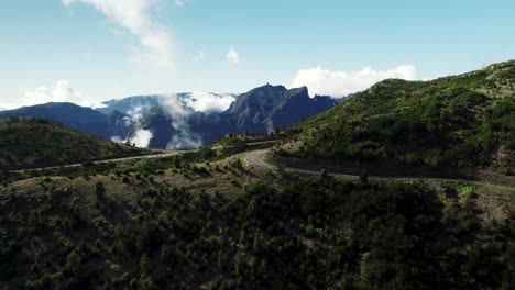 Aerial-of-Fast-Moving-Clouds,-Scenic-Road-and-Mountain-Landscape-on-Sunny-Day