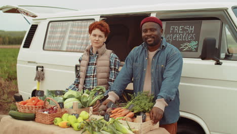 portrait of cheerful multiethnic farmers selling fresh vegetables by van