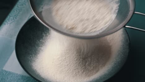 young girl sifts flour through a sieve into a baking dish, close-up view