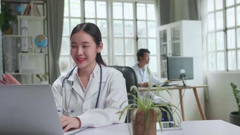 asian female doctor communicates with patient by video link, doctor consults patient using modern technologies, using laptop computer in workplace