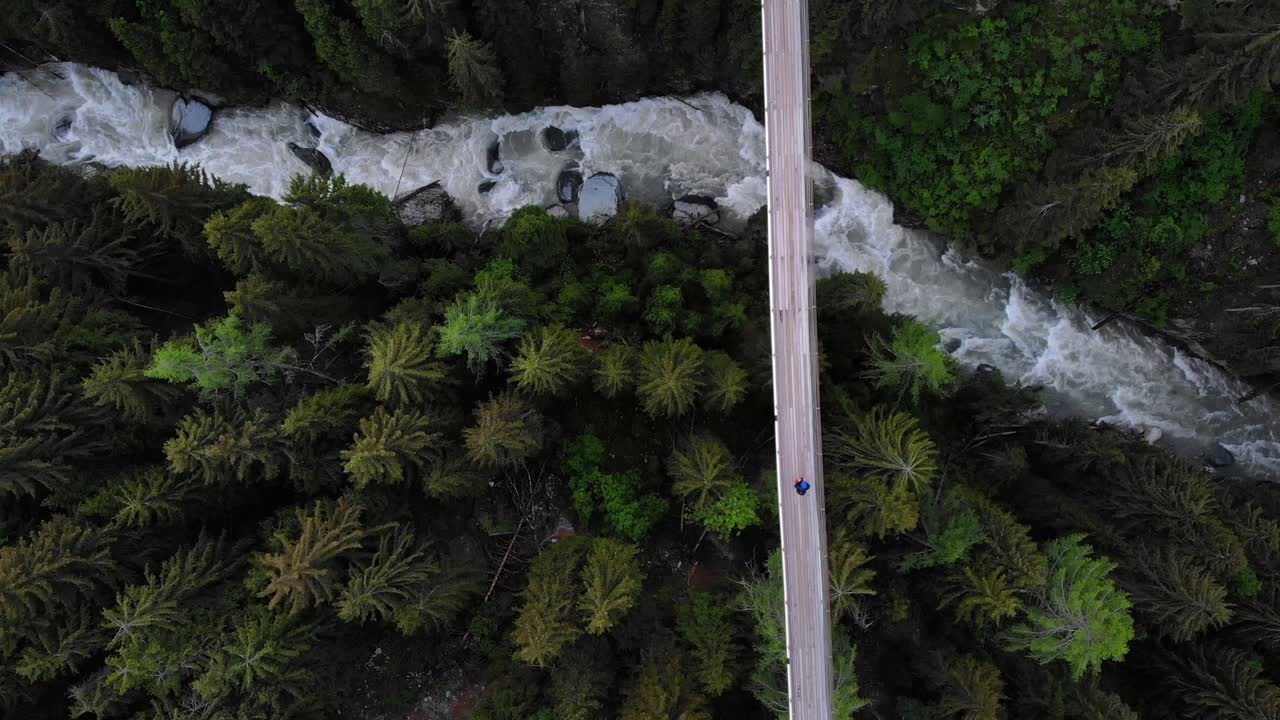 vista aérea de arriba hacia abajo siguiendo a un excursionista que cruza un puente colgante en lo alto del valle del río ródano en valais, suiza en el puente de goms