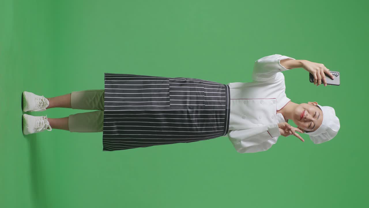 Full Body Of Asian Woman Chef Using Smartphone Taking Picture While Standing In The Green Screen Background Studio