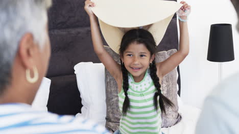 Biracial-man-with-gray-hair-is-holding-a-cushion,-partially-obscuring-a-person-behind-it