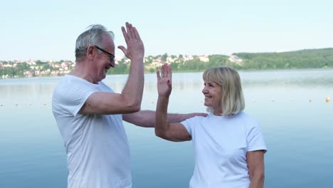 happy elderly couple by the lake high-fiving and sharing a moment