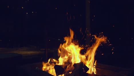 Funken-Fliegen-In-Den-Dunklen-Nachthimmel,-Während-Feuerflammen-Holz-Auf-Einem-Campingplatz-Verbrennen