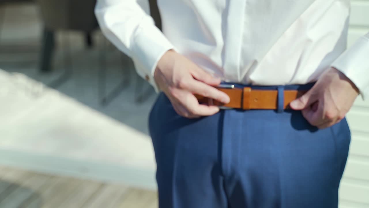 Groom Putting On Belt And Fastens It Down. Follow Shot