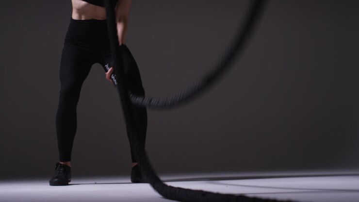 fotografía de estudio de cerca de una mujer madura con ropa de gimnasia haciendo ejercicio de cardio con cuerdas de batalla