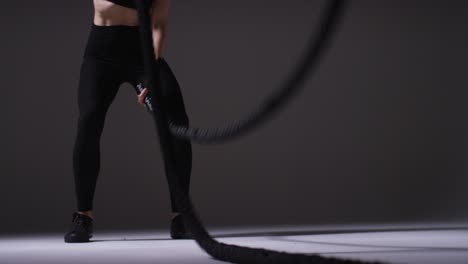 close up studio shot of mature woman wearing gym fitness clothing doing cardio exercise with battle ropes