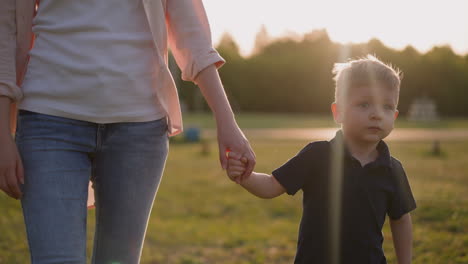 Toddler-boy-with-mother-walks-along-field-at-rural-site