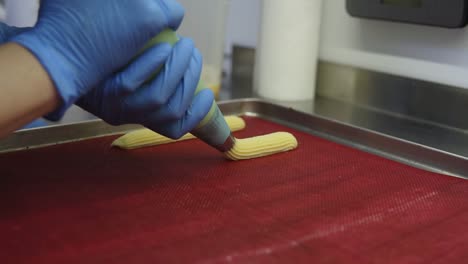 Spreading-brewed-dough-from-a-confectioners-tube-on-a-baking-surface.-Baking-tray.-Process-of-making-profiteroles-or-eclaires.-Close-up-footage