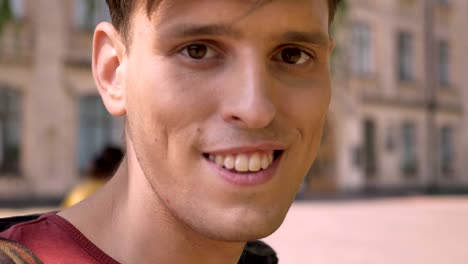 joven apuesto está viendo en el teléfono inteligente en el día en verano, viendo en la cámara, concepto de comunicación, fondo borroso