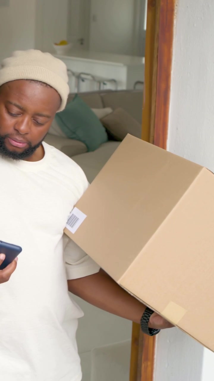 Vertical video: Reaching home door man in beanie holding box, tilting label and scanning on phone