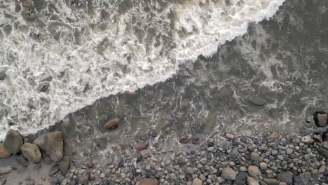 Overhead-pan-shot-of-gentle-shoreline-waves-crushing-into-the-rocky-coast