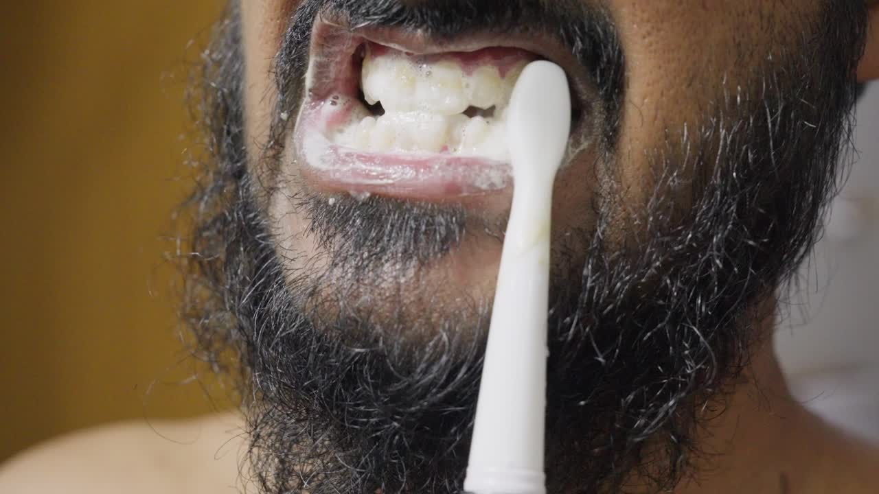 A slow-motion, close-up footage of a South Asian man brushing his teeth, with a blurred background. Dental care and hygiene concept
