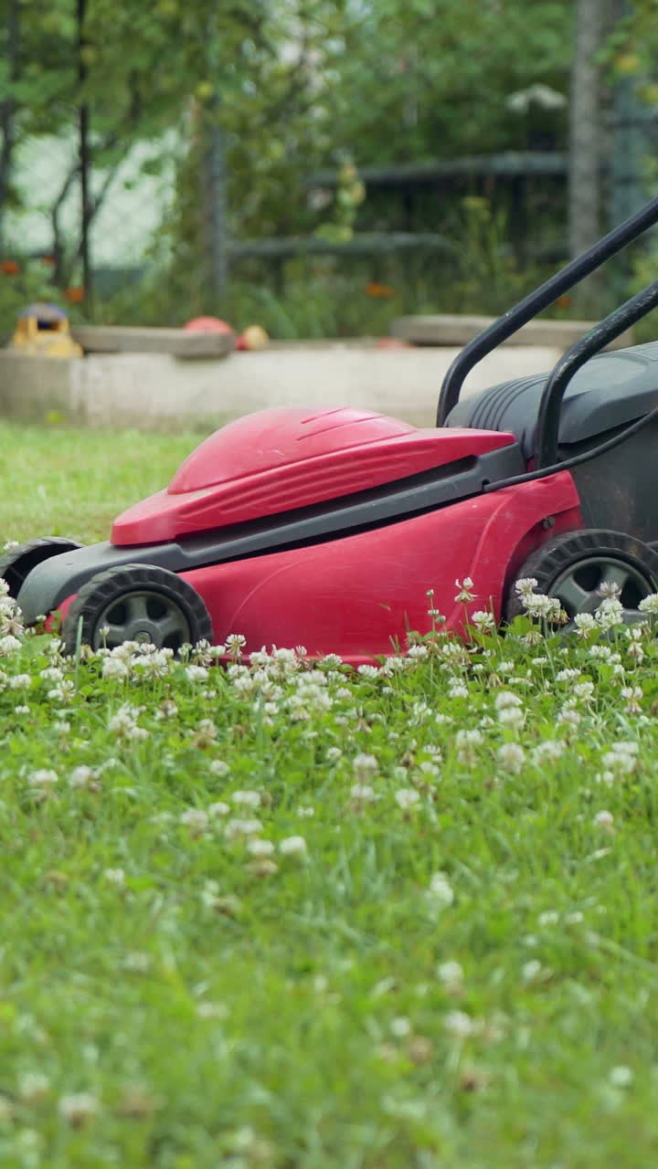 Boy running with a lawn mower in the garden. Close-up. Vertical video