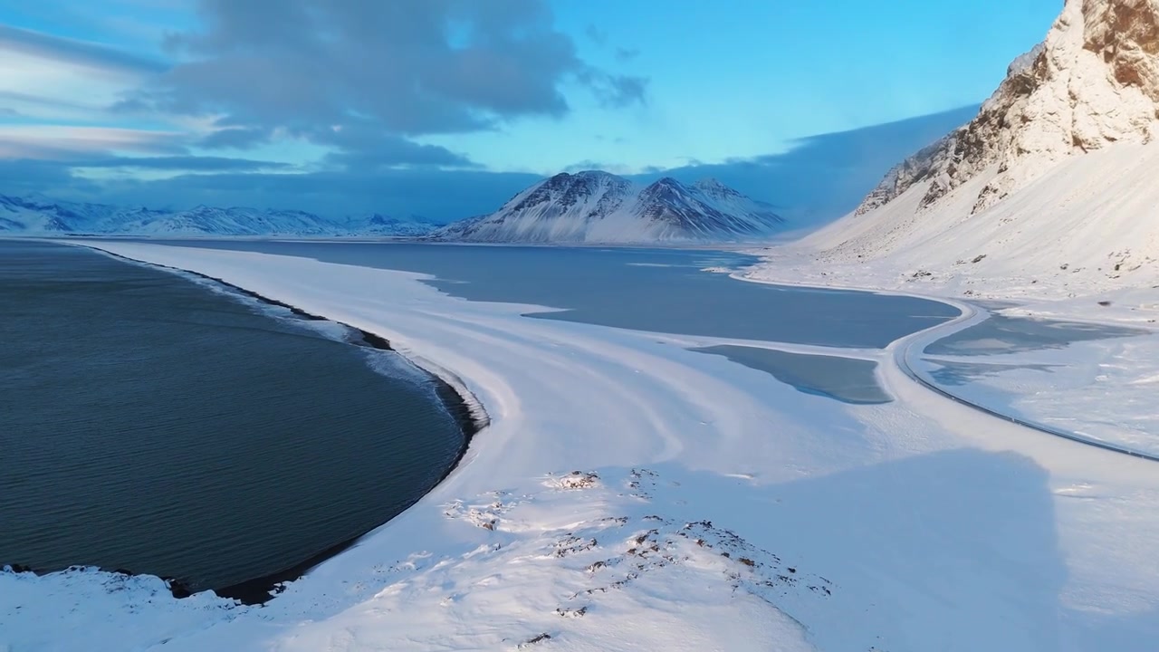 Luftfoto af sneklædte bjerge og frossen kyst i Østisland