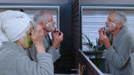 la abuela mayor aplicando una máscara facial y el abuelo afeitándose con una cuchilla de afeitar manual en el baño