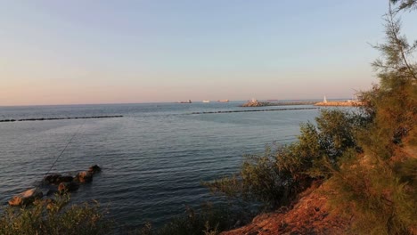 Zygi harbor opening seen from the shore in Cyprus, with a fishing rod waving gently on the beach below—capturing tranquil seaside life, harbor access, and coastal fishing culture.
