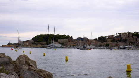 boats lying in the small marina of port d’sóller, mallorca, with mountains and forest in the background and some rocks in the foreground