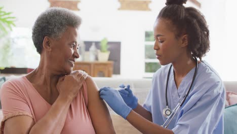 une femme médecin afro-américaine donne une injection à une femme âgée afro-américaine à la maison.