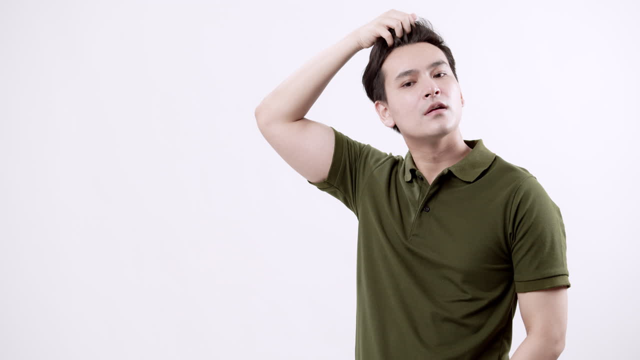 Stroking his head gently, a young man is combing his hair with his fingers.