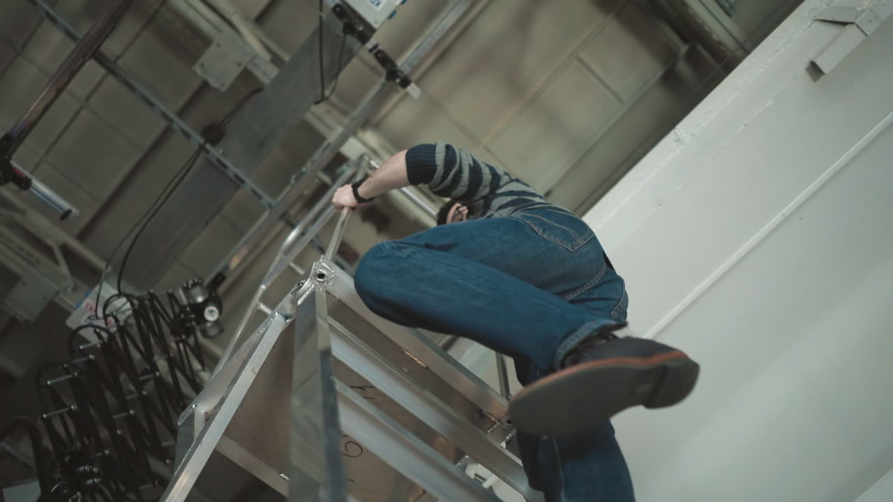Worker climbing metal ladder in studio, adjusting lighting equipment, filming environment setup, technical production, focus on crew tasks in broadcast studio