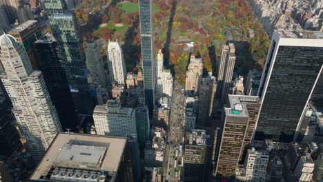 High-angle-view-of-wide-avenue-between-tall-skyscrapers.-Tilt-up-reveal-autumn-Central-park-in-middle-of-town-development.-Manhattan,-New-York-City,-USA