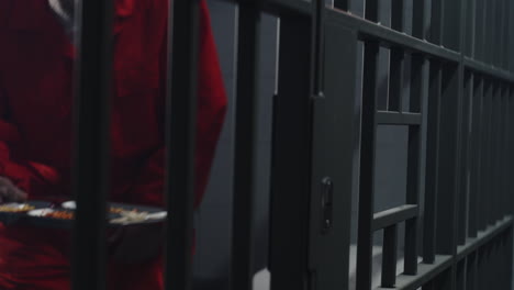 Close-Up-of-Prisoner-in-Orange-Uniform-Holding-Metal-Bars-in-Prison-Cell----------(Stock-Footage)