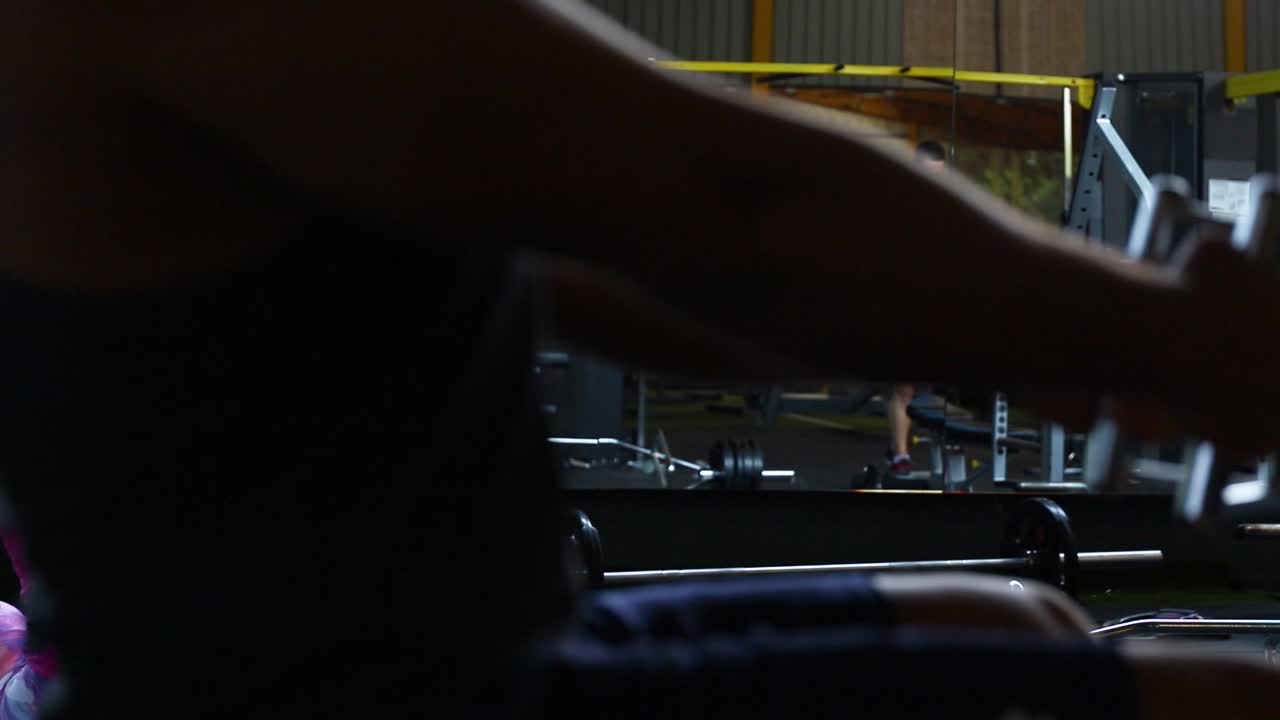Caucasian man sitting on workout bench in gym pulling weights towards chest working upper body, close up pan