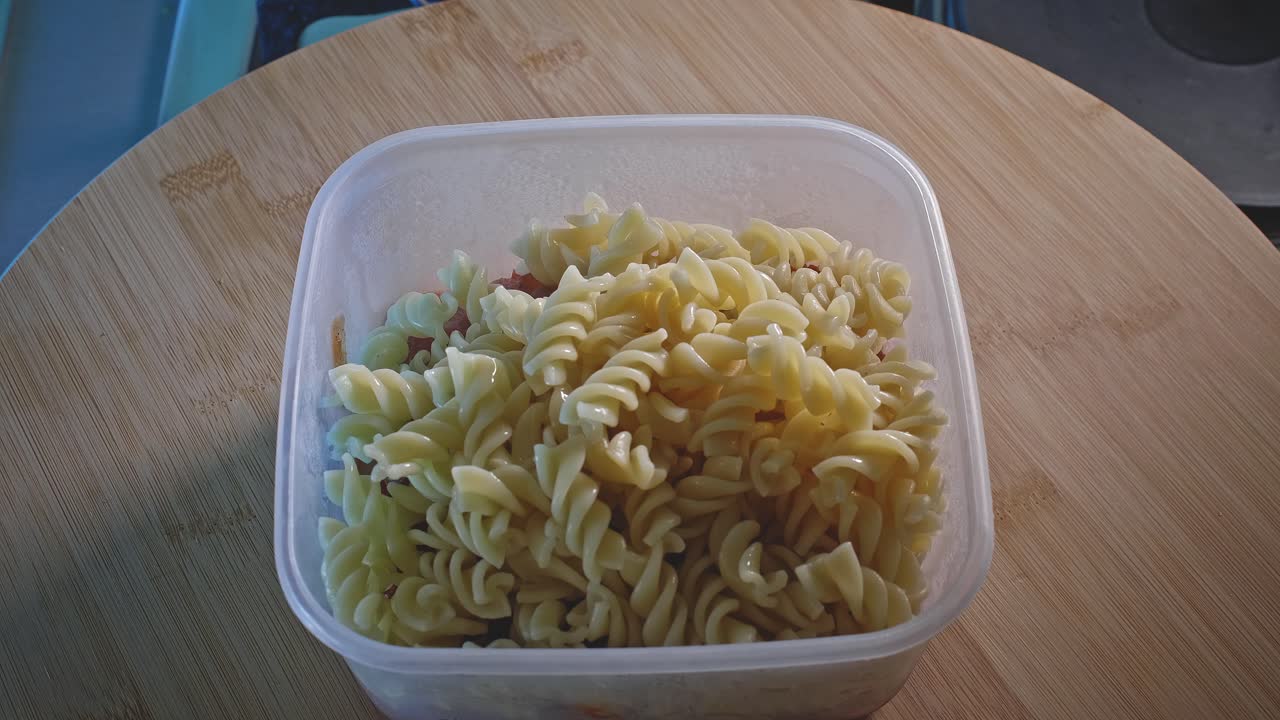 agregar pasta fusilli cocida al pollo picante con frijoles en un recipiente de plástico para alimentos