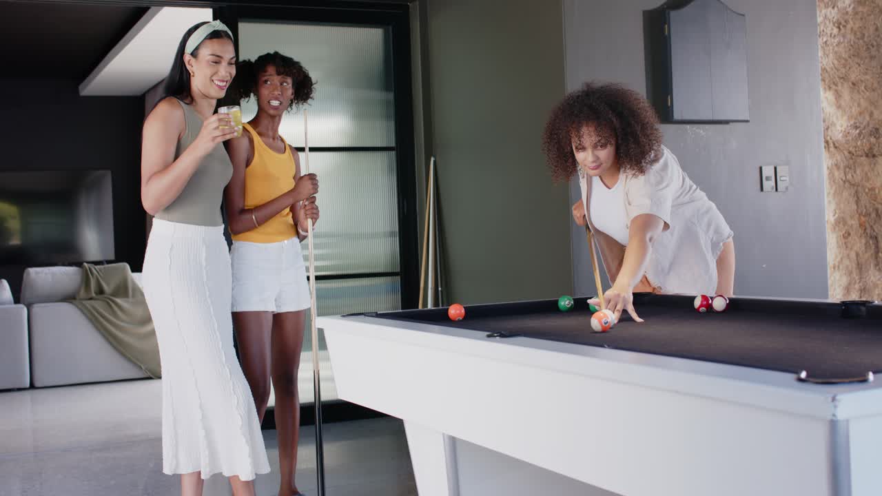 Amici afroamericani che guardano un giocatore lanciare la bilia battente su un tavolo da biliardo nero in una sala giochi.