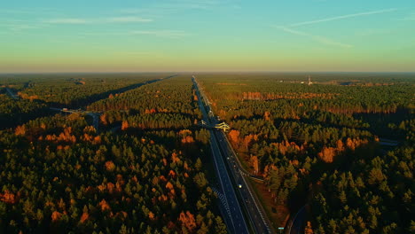 Wunderschöne-Luftaufnahme-Eines-Farbenfrohen-Waldes-Und-Einer-Autobahn,-Die-Durch-Ihn-Verläuft,-Mit-Einem-Atemberaubenden-Horizont-Und-Himmel-Mit-Vielen-Blautönen