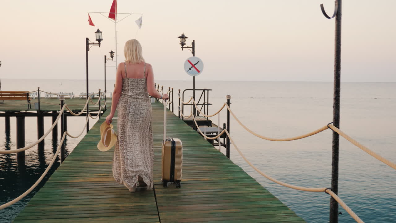 A Woman With A Bag On Wheels Rides The Pier Towards The Sea The Rising Sun Beautifully Illuminates H