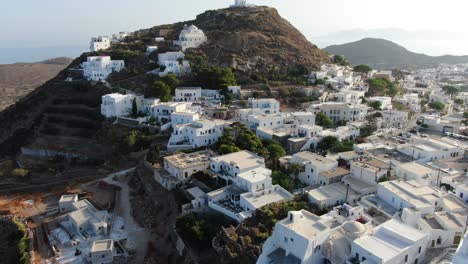 Vista-De-Drones-En-Grecia-Volando-Frente-A-Una-Ciudad-Griega-Con-Casas-Blancas-En-Una-Colina-Marrón-Con-Una-Iglesia-En-La-Cima-Y-El-Mar-En-El-Horizonte-En-Un-Día-Soleado