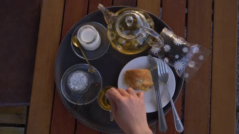 pov woman hand mix tea in a glass cup on a tray with muffin and milk