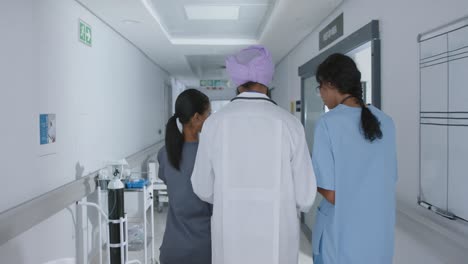 Diverse-doctors-and-nurse-talking-and-walking-through-corridor-at-hospital,-in-slow-motion