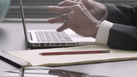 left handed executive takes written notes and types on a laptop at his desk still shot