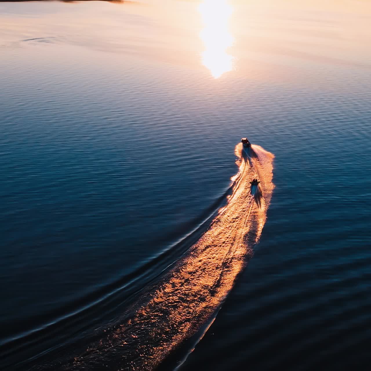Motor boat on water at sunset. Panoramic view of the evening river with two boats. Motor boat pulling small boat with people. View from above.