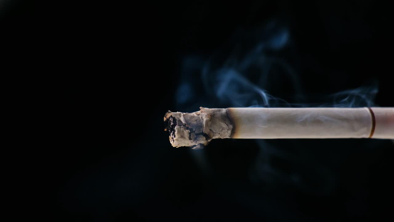 un cigarrillo fumando con fondo negro las cenizas y el humo son visibles con luz suave en el cigarrillo