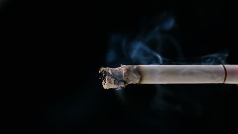 a cigarette smoking with black background ashes and smoke are visible with soft light on the cigarette