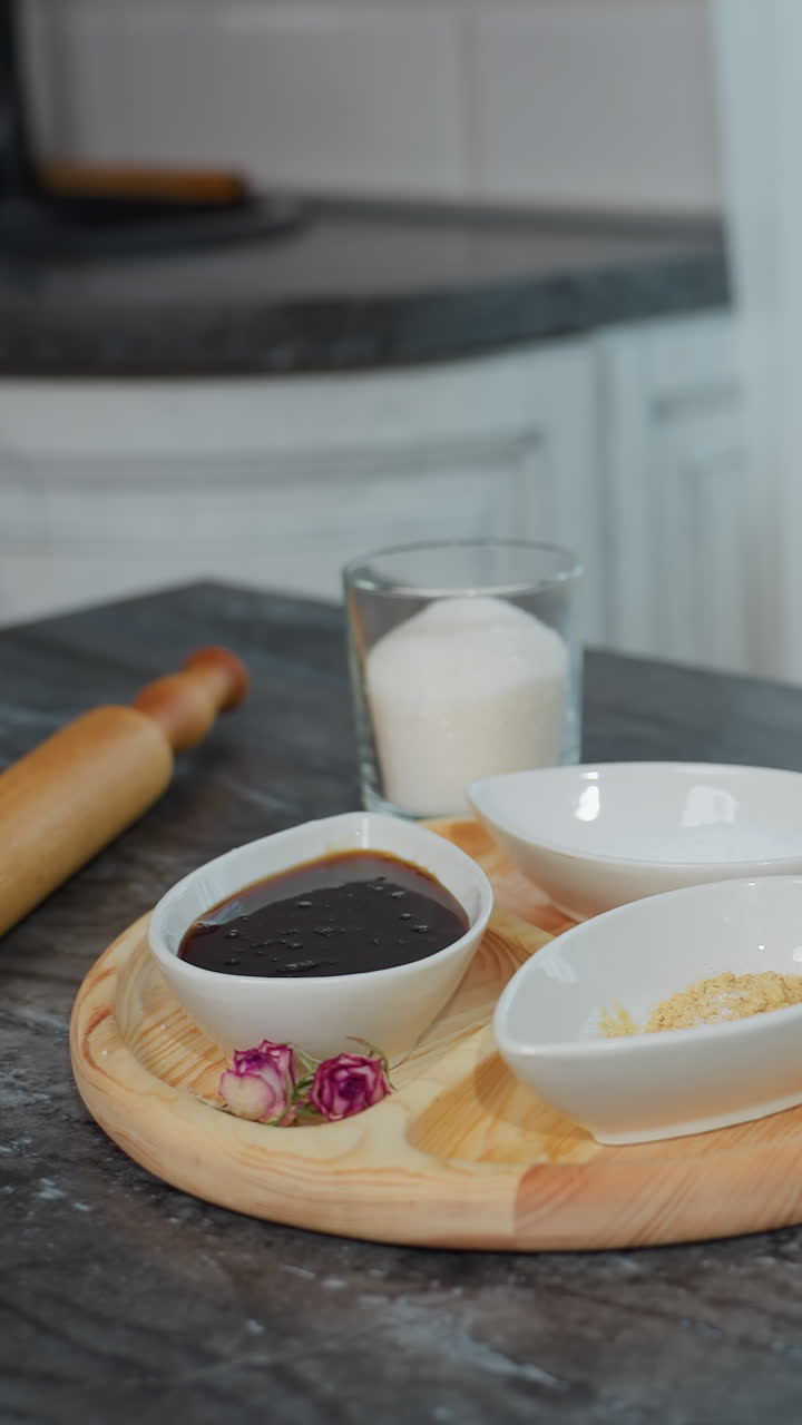 miel en platos en una bandeja de madera con artículos esenciales de la cocina, azúcar, mantequilla y rodillo en una elegante mesa negra, la cortina blanca permite la luz natural suave, revelando el edificio nevado a través de la ventana