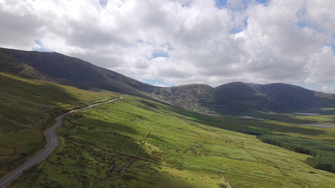 Una vasta ripresa aerea dell'iconico Conor Pass a Dingle, Irlanda, che mostra una strada di montagna tortuosa attraverso valli verdi lussureggianti sotto un cielo nuvoloso