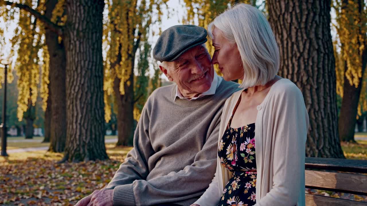 A warm, intimate video scene of an elderly couple sitting on a park bench, captured from a side