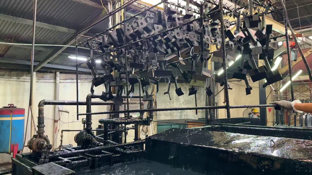 O ferro pendurado no suporte é colocado em uma cuba contendo líquido químico de tinta preta usando um guindaste. Processo de pintura por eletrodeposição. Pintura preta.