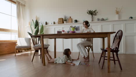 Wide-Shot-Of-A-Mother-Making-A-Videocall-While-Her-Daughter-Is-Distracted-Under-The-Table-Drawing-2