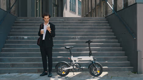 businessman with e-bike, coffee, and phone in urban setting